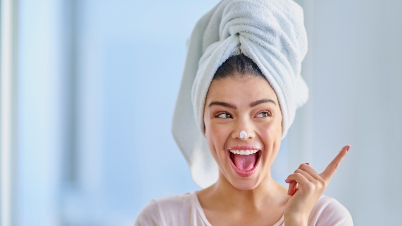Žena sa peškirom na glavi i kremom na nosu, spremna za jutarnju beauty rutinu