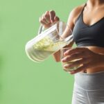 prikaz devojke koja sipa u čašu detoks sok iz bokala, pozadina zelena sa kivijem, spanaćem i limunom